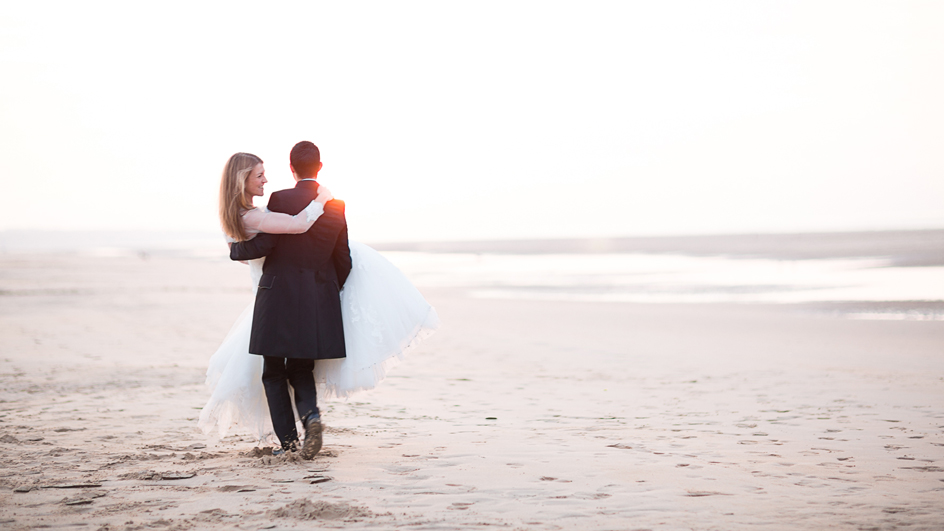 Photographe mariage Caen : Le marié portant la mariée day after sur la plage de Colleville sur mer